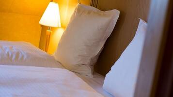 A neatly made bed with white linens and pillows, a bedside lamp, and a wooden headboard.