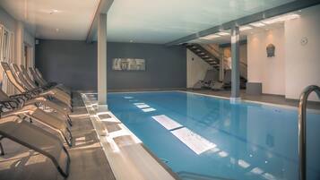 A swimming pool with sunlit water, lounge chairs, and a Buddha statue.