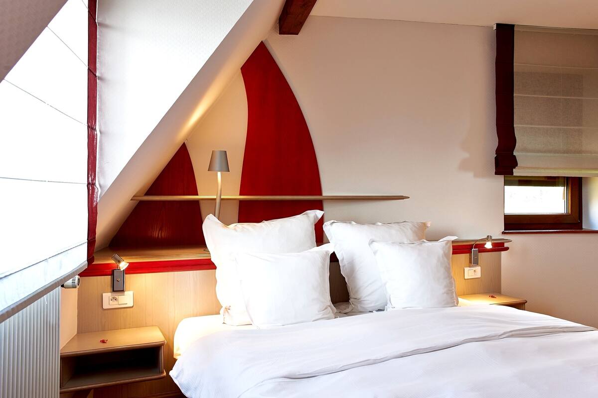 A hotel room with a bed, bedside tables, a lamp, and a window.
