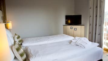 Habitación de hotel con dos camas, un televisor sobre un mueble de madera y una ventana con cortinas.