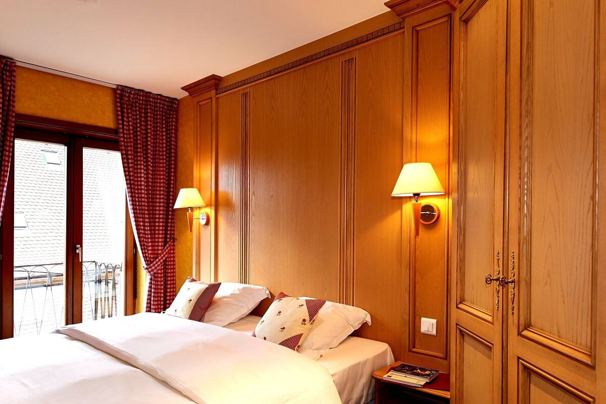 A hotel room with two beds, wooden paneling, and two wall-mounted lamps.