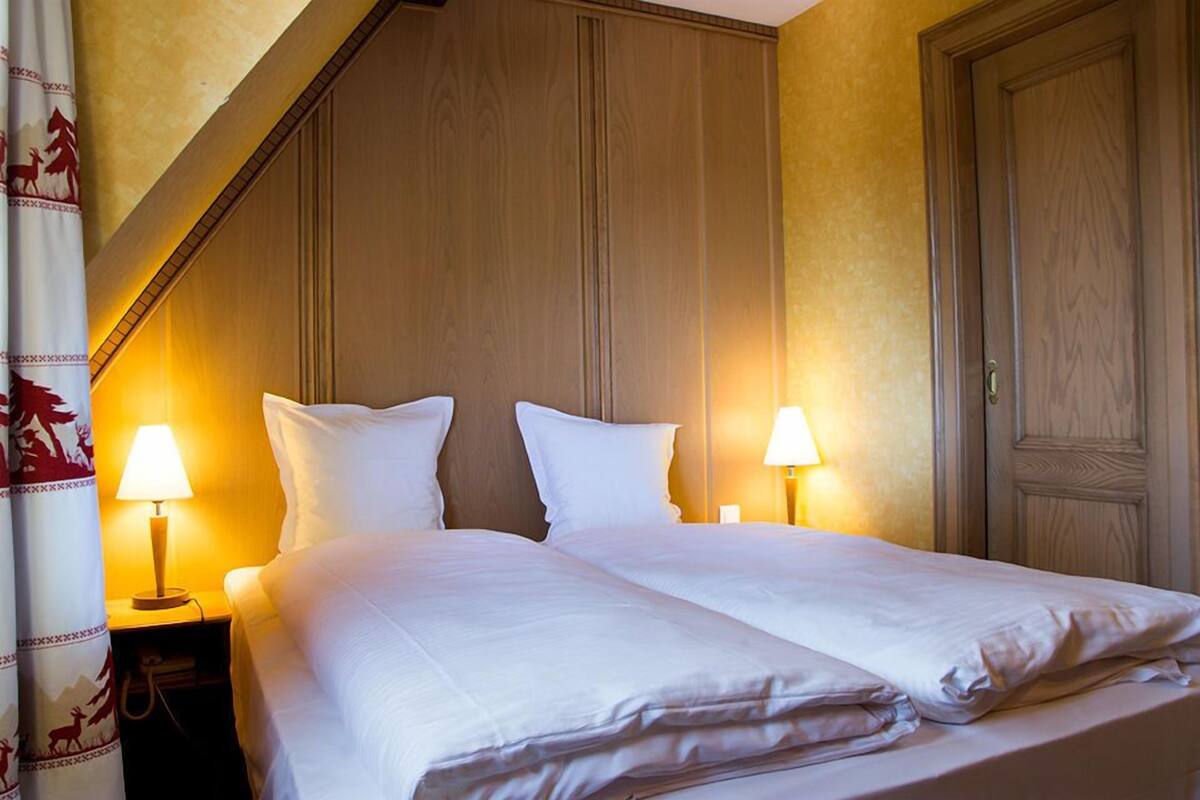 A double bed with white linens, two bedside lamps, and a wooden headboard.