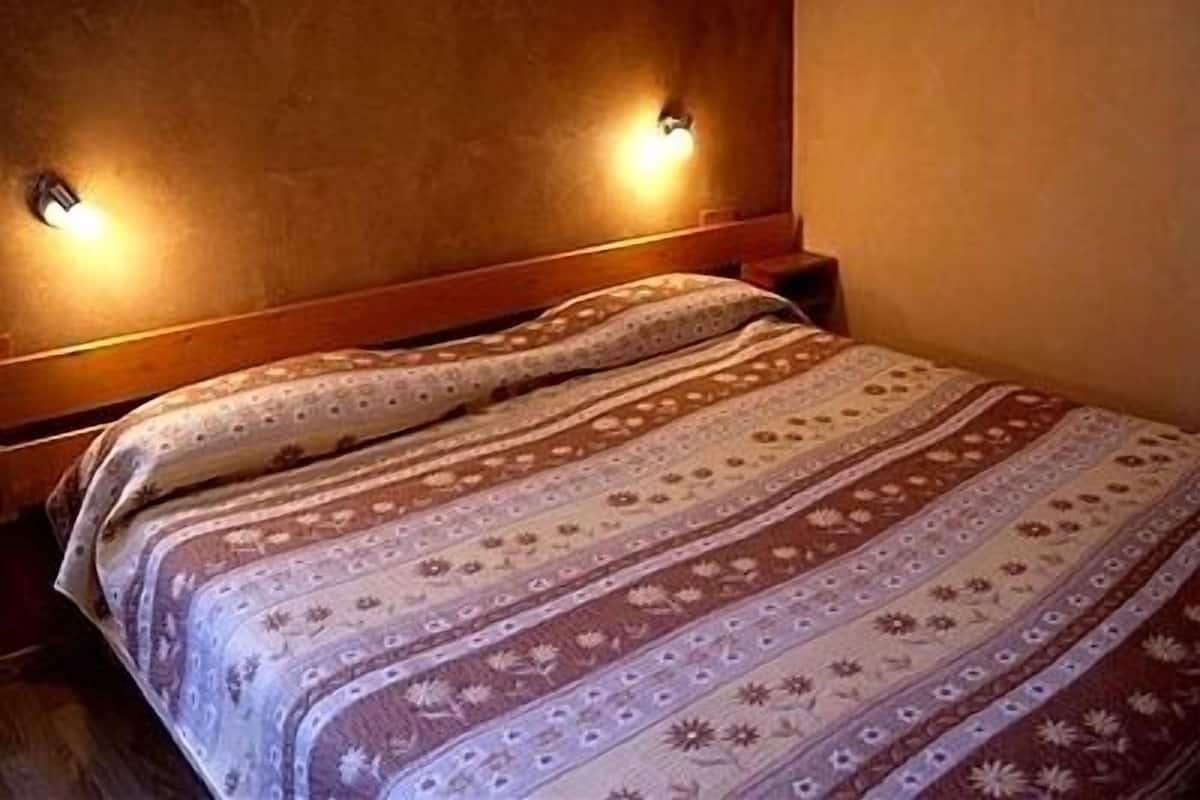 A bed with a patterned bedspread and two wall-mounted lights.