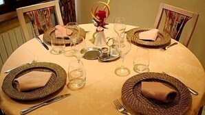Una mesa de comedor redonda con individuales tejidos, servilletas dobladas y cristalería transparente.