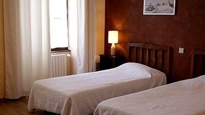 Una habitación con dos camas individuales, un radiador, una lámpara y un cuadro en la pared.