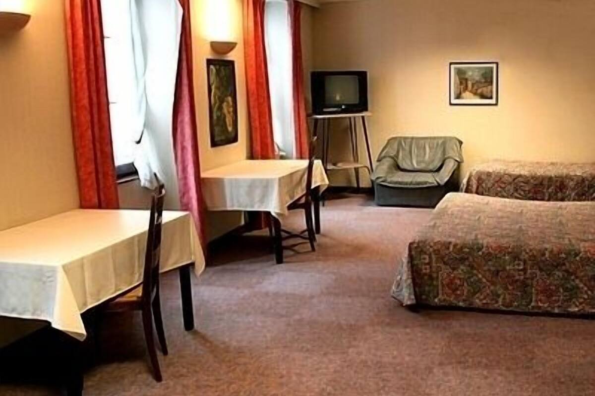 A hotel room with a bed, a table, two chairs, a television, and a painting on the wall.