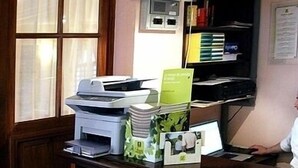 Un mostrador de recepción con una impresora, una pila de carpetas verdes y un monitor de computadora.