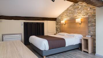 Un dormitorio con cama, mesita de noche de madera, pared de piedra y techo con vigas a la vista.