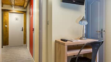 A hotel room with a wooden desk, a chair, a desk lamp, and a television mounted on the wall.