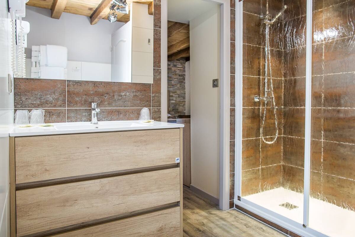 A modern bathroom with a wooden vanity, a glass shower enclosure, and a stone accent wall.
