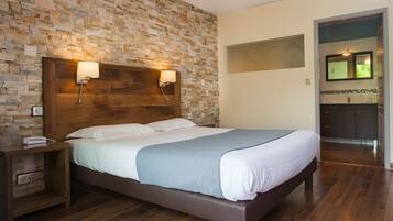 A modern bedroom with a stone wall, wooden headboard, bedside lamps, and a view of the kitchen.