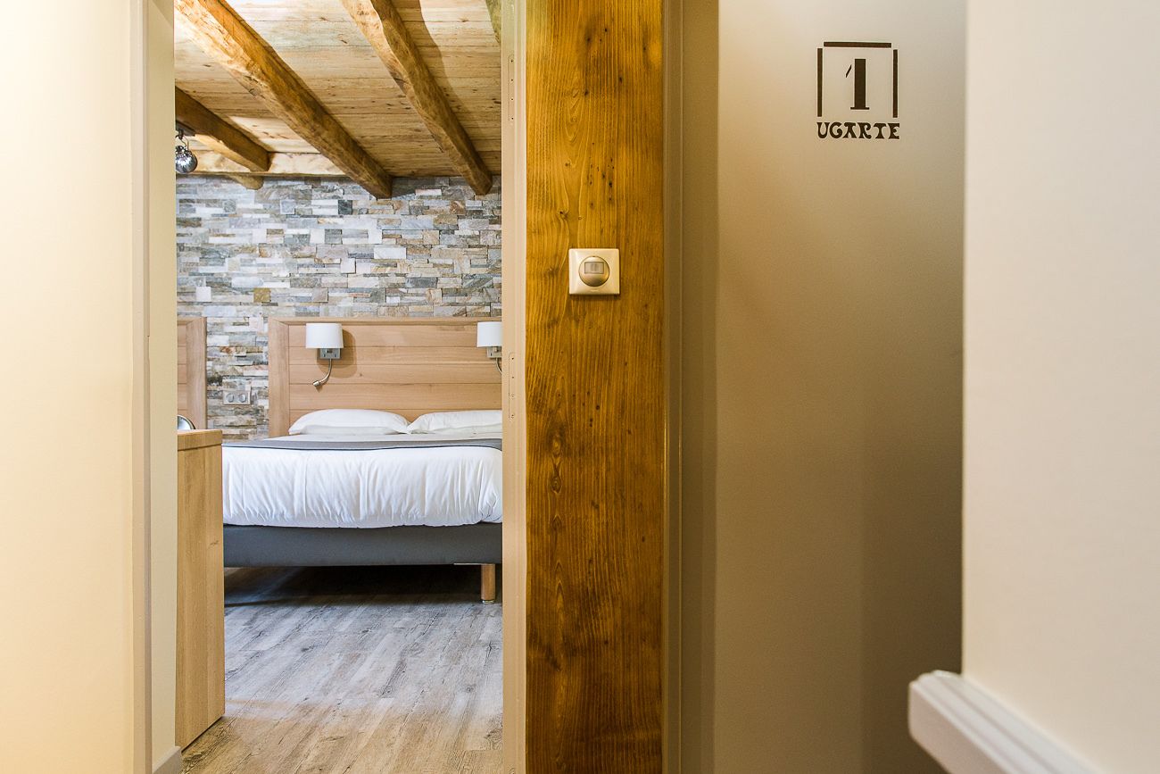 Une chambre avec un mur en pierre, des poutres apparentes en bois au plafond, un lit avec une literie blanche et une porte dotée d’une serrure.