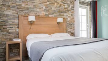 Una cama bien hecha con cabecera de madera, una mesita de noche con lámpara y una pared con diseño de piedra.