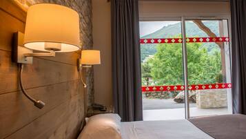 A hotel room with a wooden wall, two bedside lamps, a bed, and a view of a mountainous landscape through a glass door.