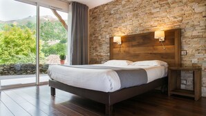 Un dormitorio con una cama grande, cabecera de madera, pared de piedra y vistas a la vegetación a través de una puerta corrediza de vidrio.