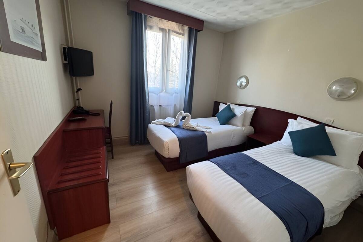 A hotel room with two beds, a desk, a TV, and a window with curtains.