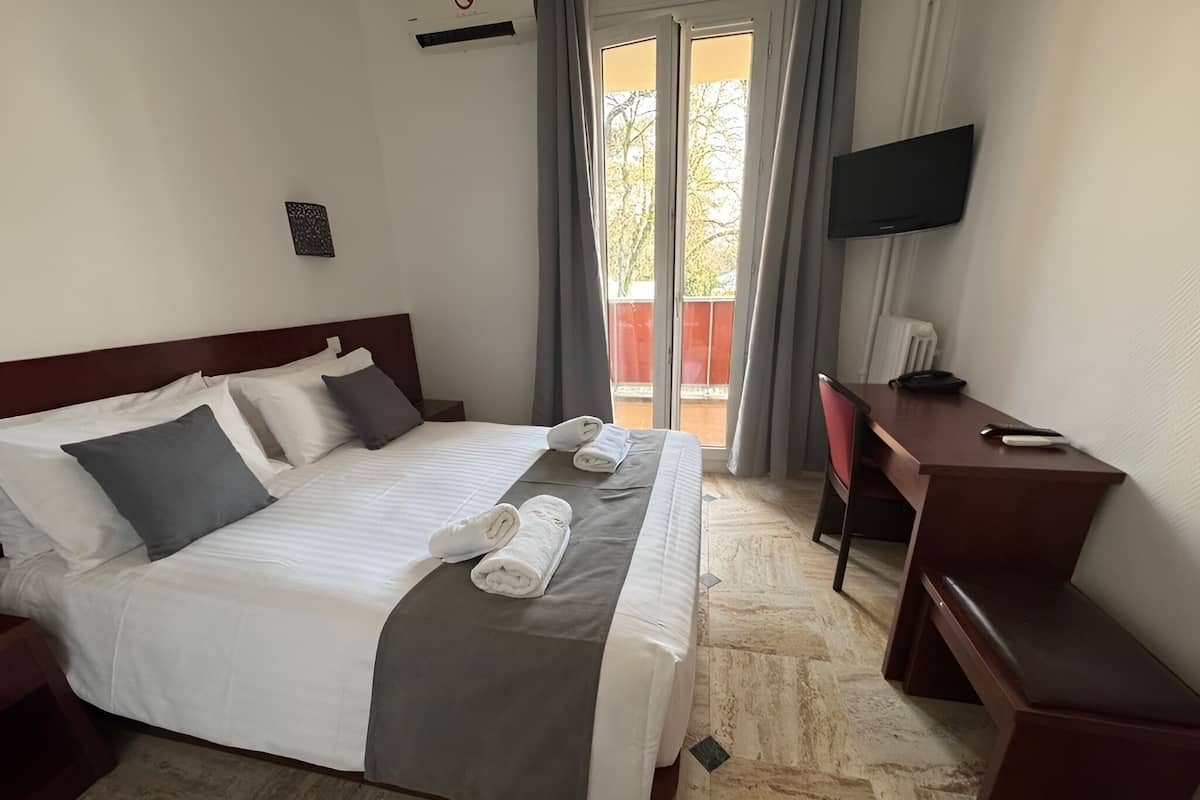A hotel room with a bed, a desk, a chair, a TV, and a view of the outdoors.