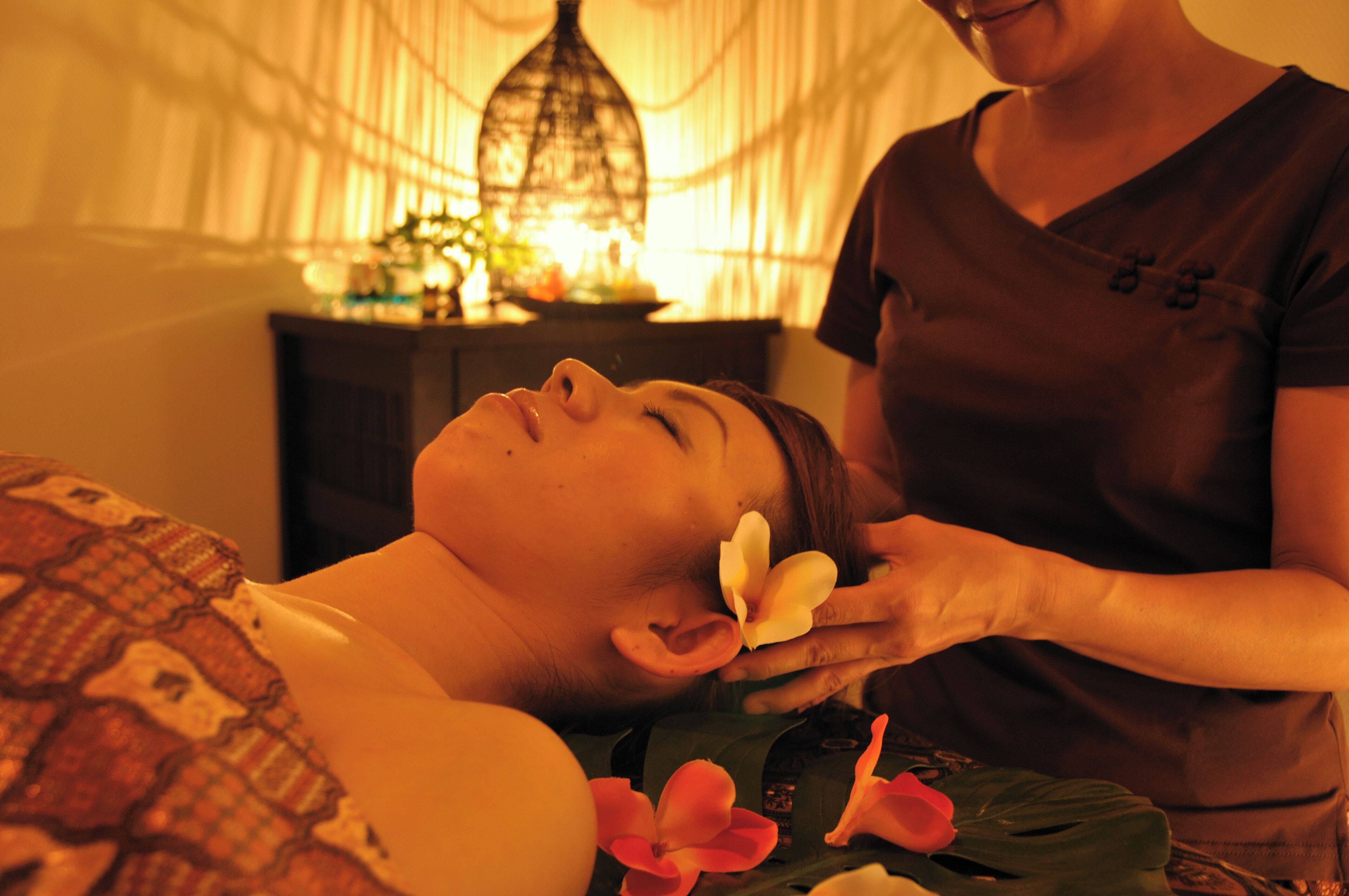 A person receiving a massage in a room with a bed, a nightstand, and a decorative lamp.