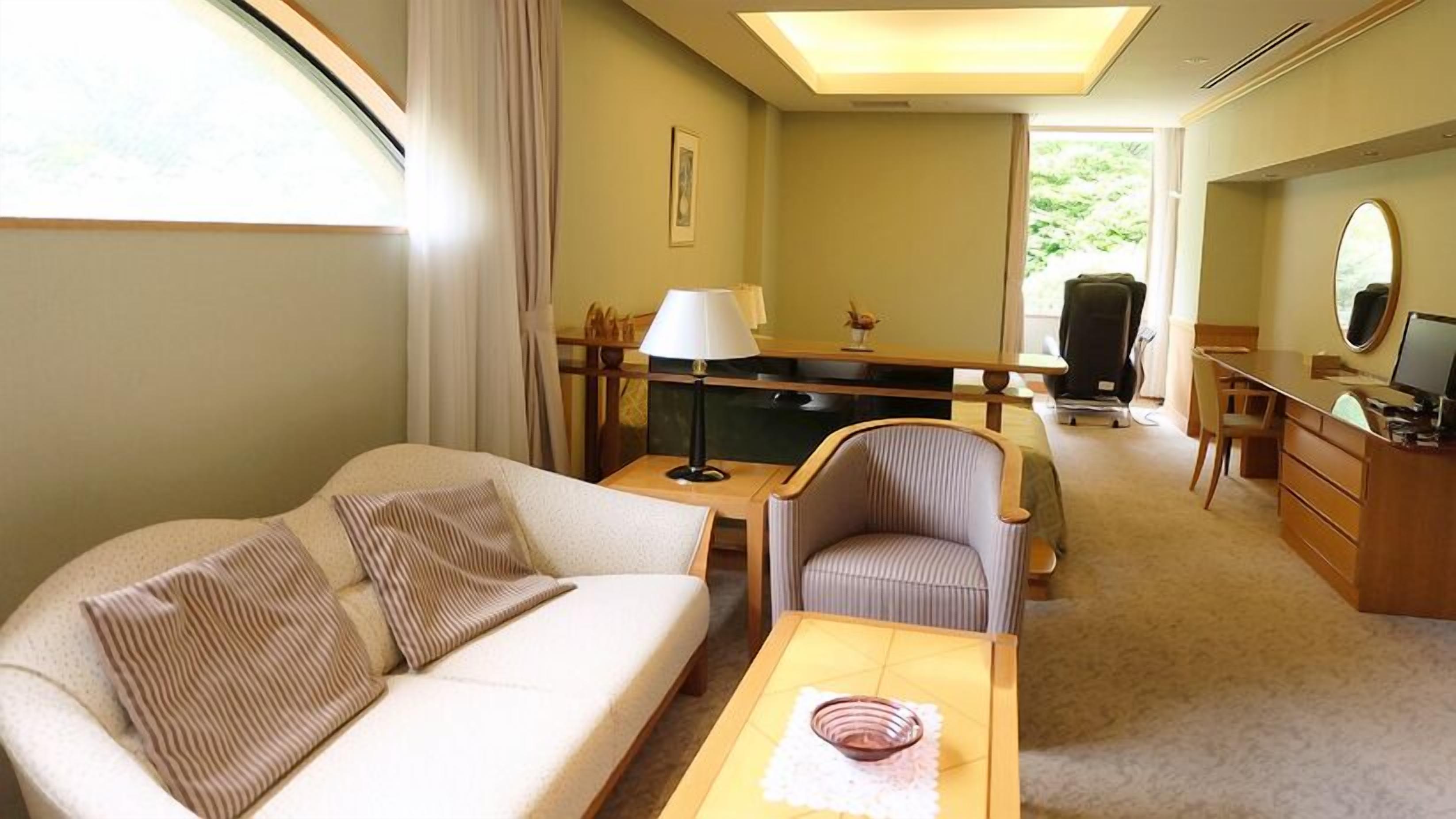 A hotel room with a sofa, a desk, a chair, a lamp, a television, and a window with curtains.