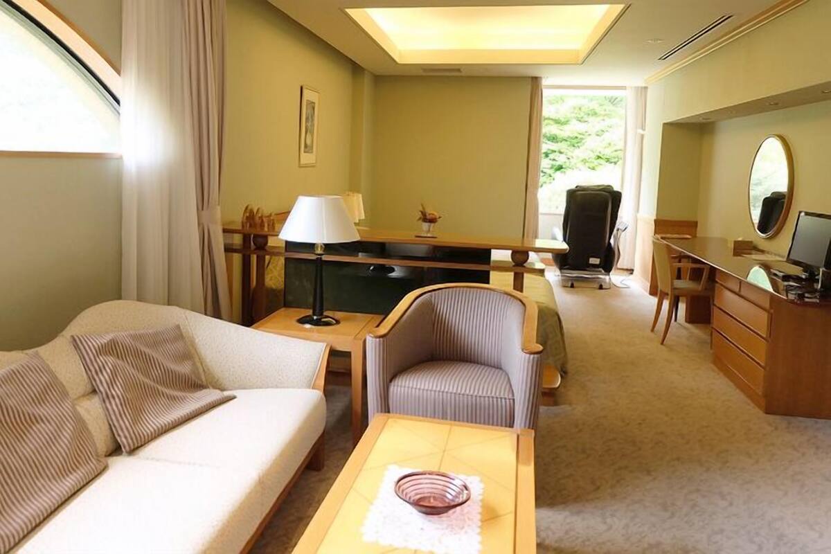 Hotelkamer met een bank, bureau, stoel, lamp, televisie en een raam met gordijnen.
