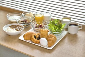 A breakfast tray with croissants, eggs, and a salad on a wooden table near a window with blinds. - R&B Hotel Tokyo Toyo-cho (Tokyo)