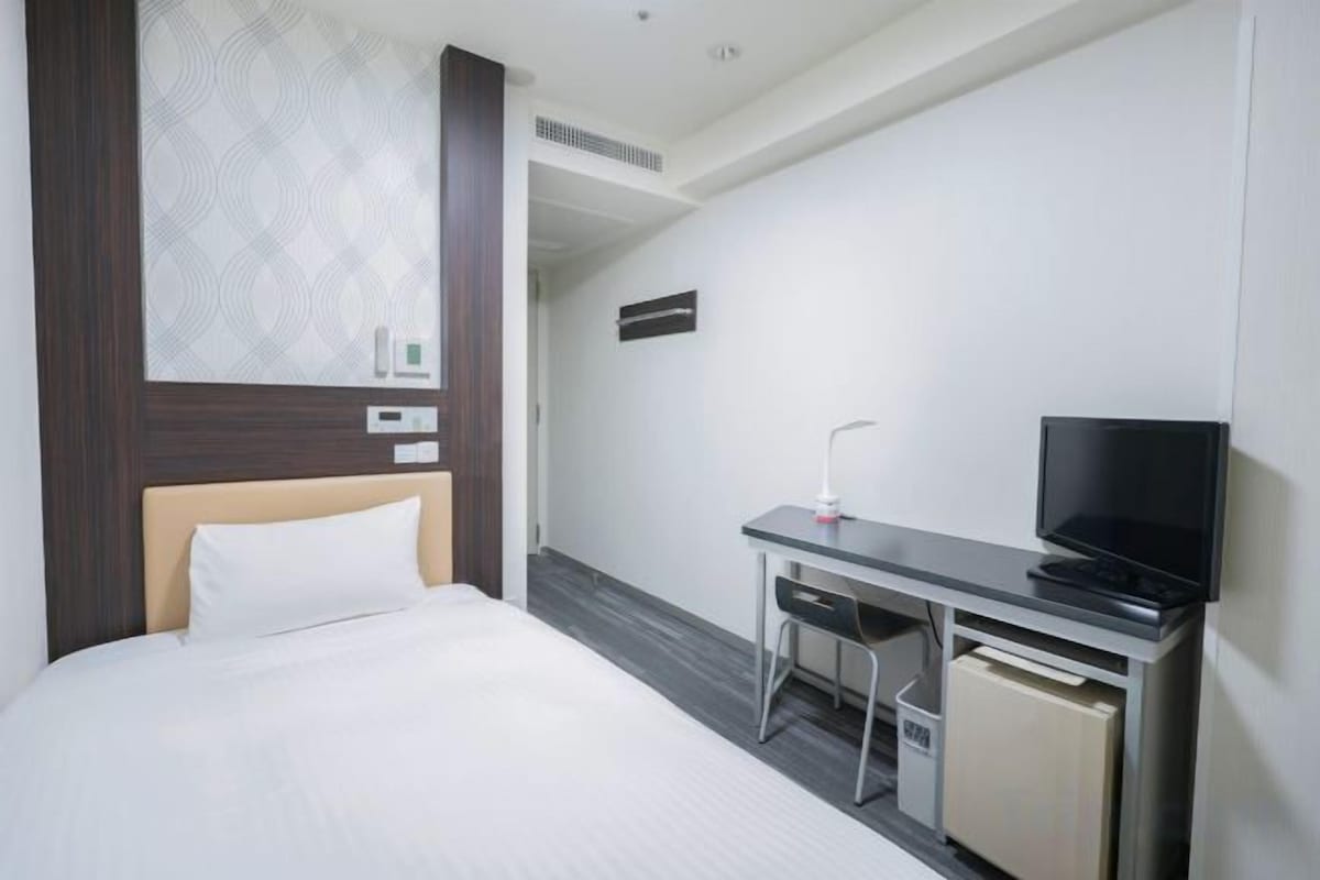 A hotel room with a bed, a desk with a television, and a small cabinet.