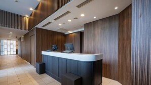 A modern reception desk with a curved design, flanked by wooden paneling and a tiled floor. - R&B Hotel Tokyo Toyo-cho (Tokyo)