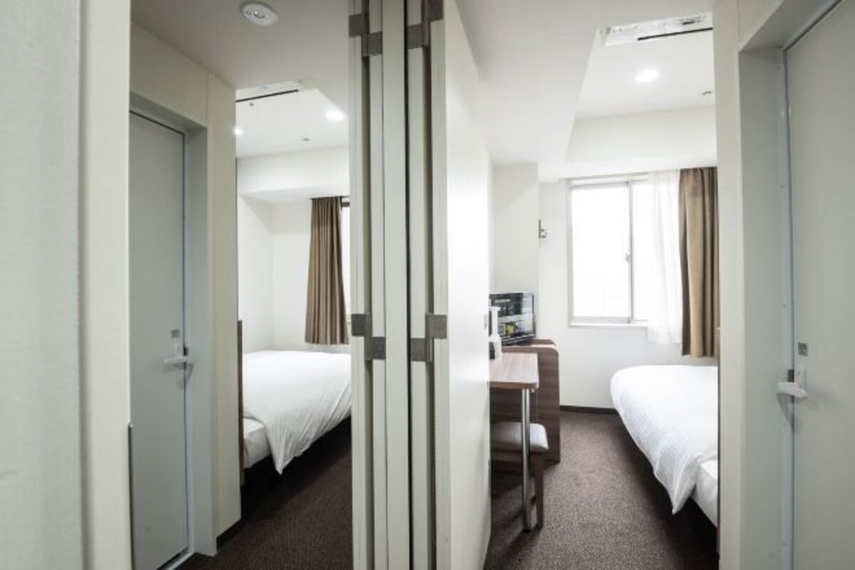 A hotel room with two beds, a desk, and a window.