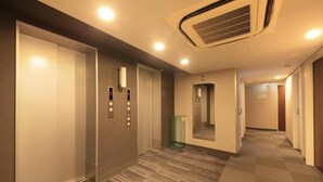 A hotel corridor with a carpeted floor, a mirrored wall, and an elevator with a control panel. - R&B Hotel Tokyo Toyo-cho (Tokyo)