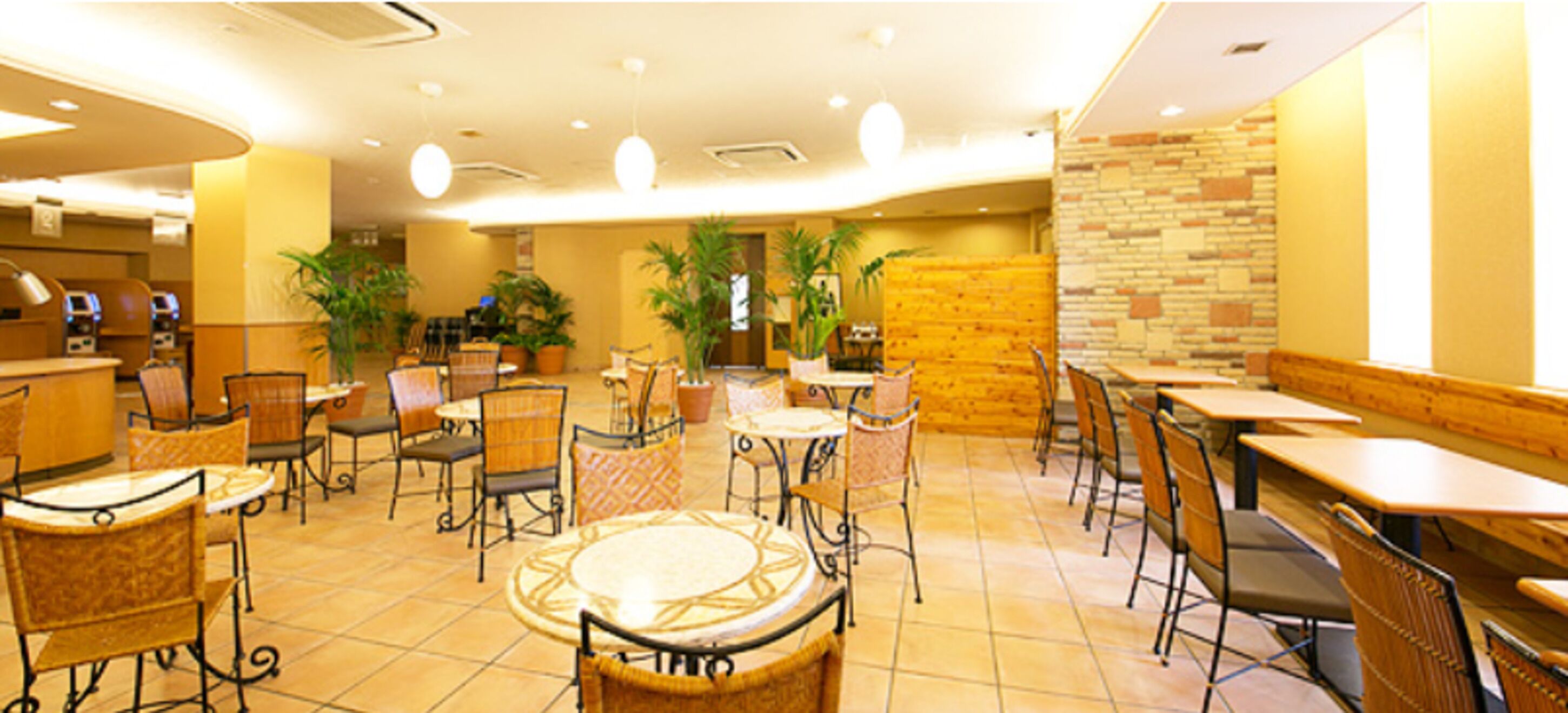A restaurant with round tables and chairs, potted plants, and a brick wall.