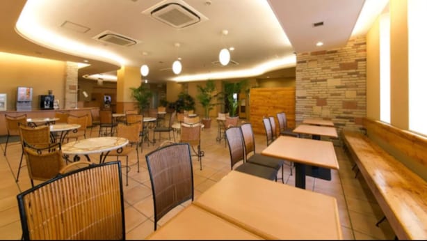 Um restaurante com mesas e cadeiras redondas, uma parede de pedra e um banco de madeira junto à parede.