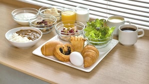 Bandeja de café da manhã com croissants, ovos e uma salada em mesa de madeira perto de uma janela com persianas.