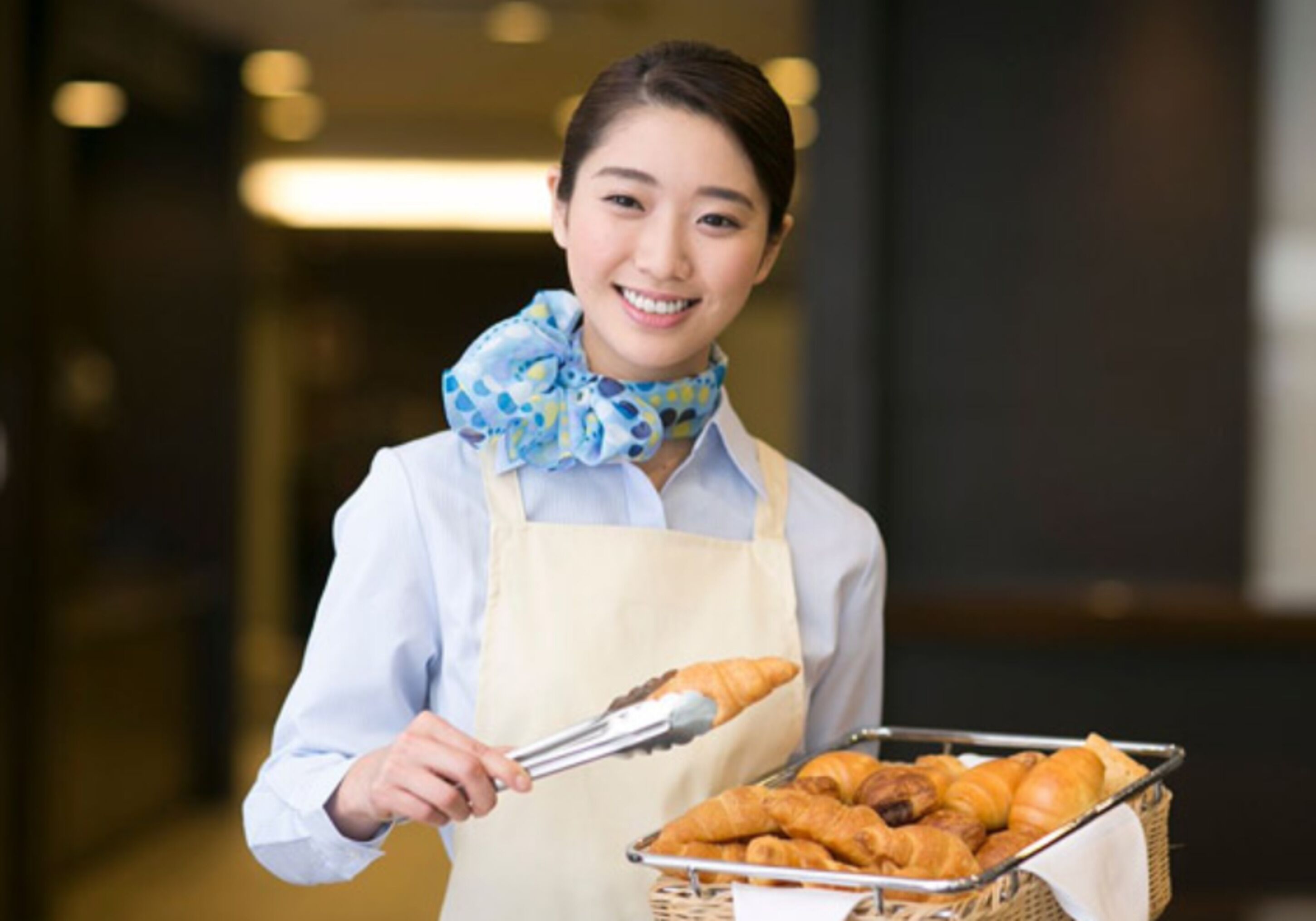 A person holding a tray with croissants and a basket of pastries.