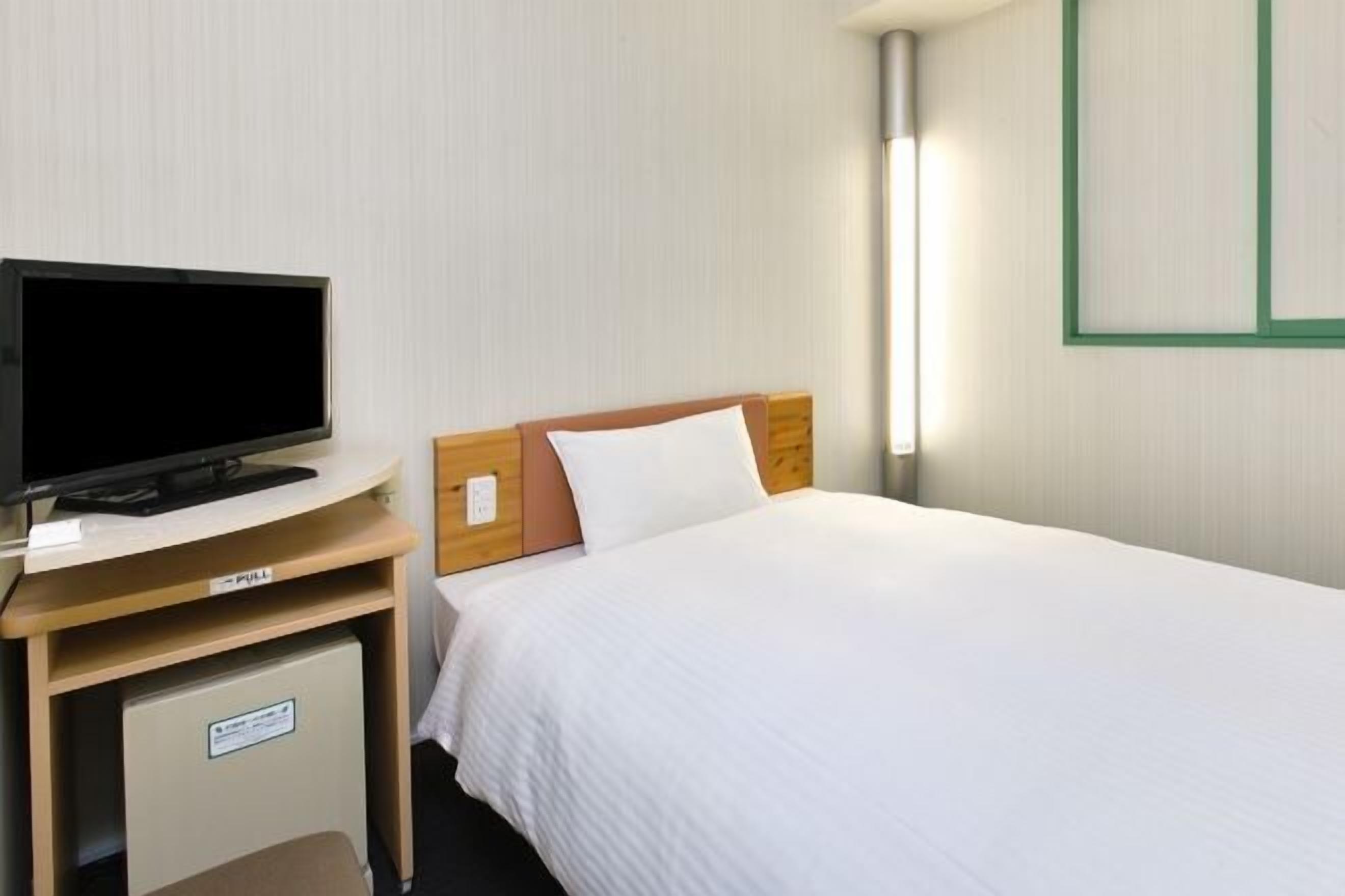 Ein Hotelzimmer mit einem Bett, einem Fernseher auf einem Holztisch und einem Nachttisch.