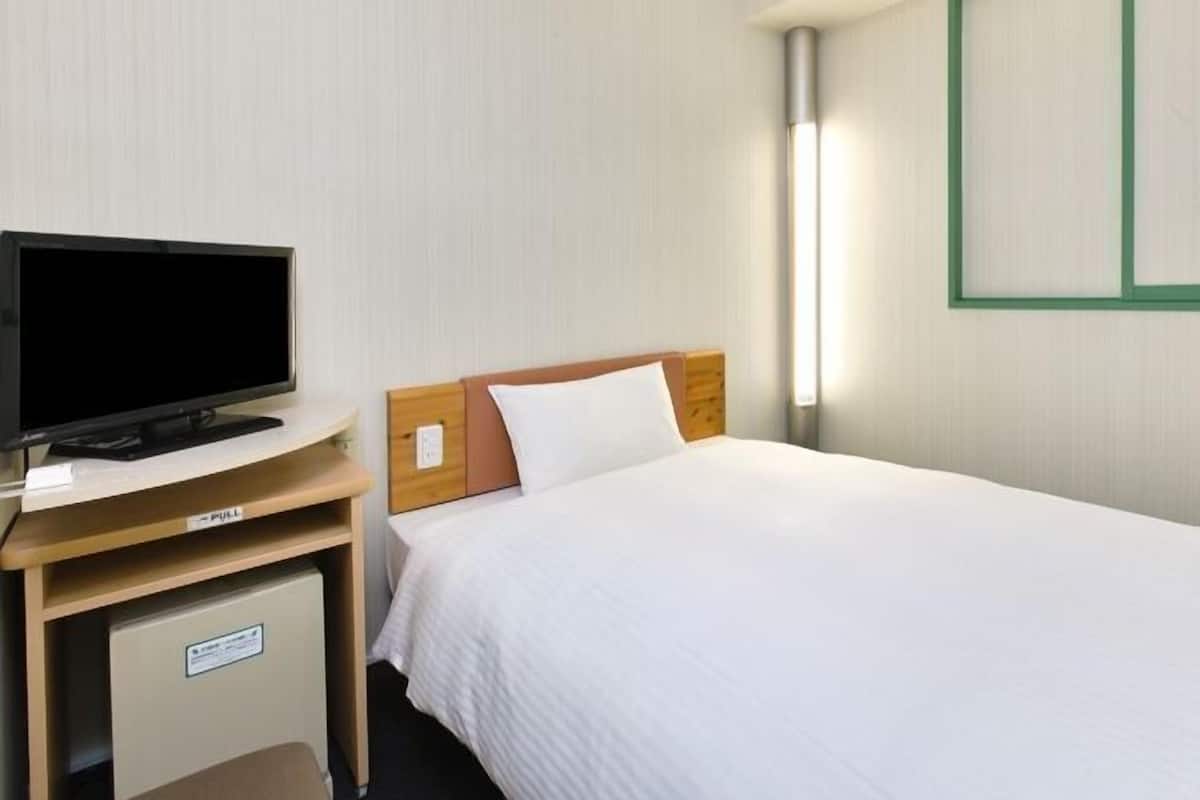 A hotel room with a bed, a television on a wooden stand, and a nightstand.
