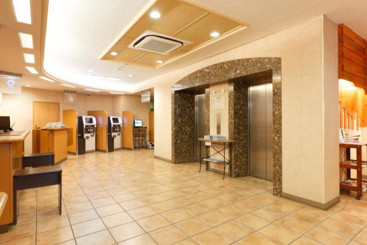 A hotel lobby with a reception desk, self-service kiosks, a seating area, and an elevator.