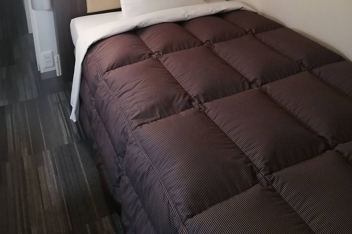Une chambre d’hôtel avec un lit, une tête de lit, un panneau de commande fixé au mur et un mur décoré d’un motif.