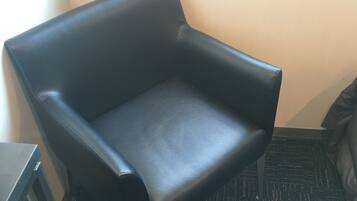 A black leather armchair in a corner of a room with a window, carpeted floor, and a small table.