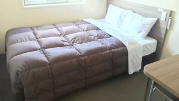A neatly made bed with a brown quilt and white pillows, a wooden nightstand, and a window with blinds.