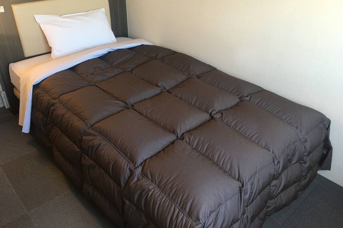 Un lit bien fait, avec une couverture marron et des oreillers blancs, dans une chambre d’hôtel.