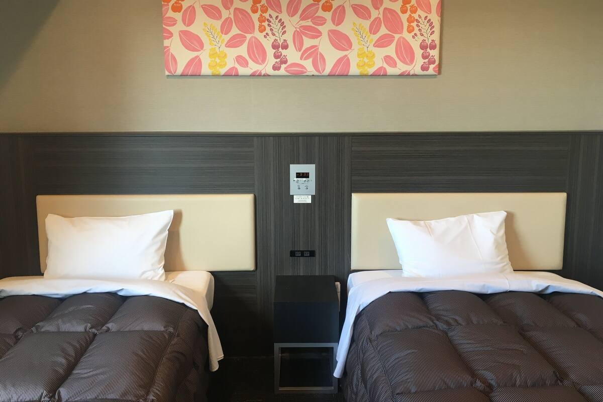 Une chambre d’hôtel avec deux lits, une grande œuvre d’art florale au-dessus des lits, un panneau de commande au mur et un petit meuble de rangement sous les lits.