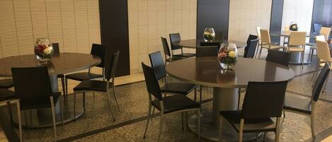 A modern hotel conference room with round tables, black chairs, and decorative vases.