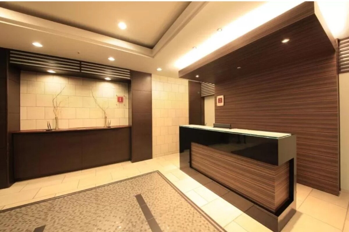 A reception area with a modern design, featuring a reception desk, a wall-mounted information board, and a tiled floor.