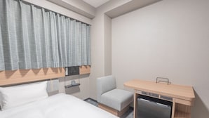 Une chambre d’hôtel comprenant un lit, un bureau avec un mini-réfrigérateur intégré, une chaise et une fenêtre avec des rideaux.