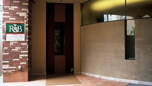 Una entrada de edificio moderna con fachada de piedra, puerta de madera y un cartel que indica R&B.