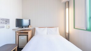 Habitación de hotel con cama, televisión sobre un mueble de madera, pequeño escritorio con ordenador y luz de pared.