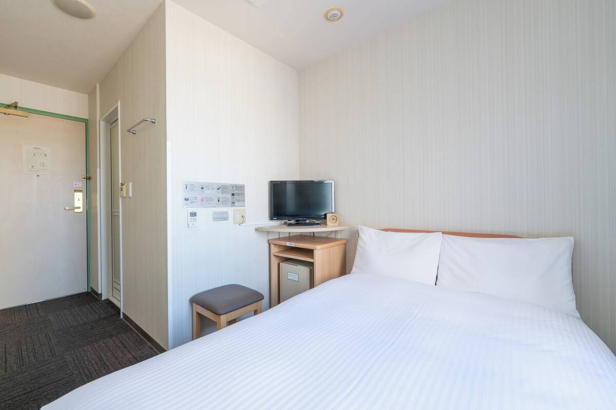Una habitación de hotel con una cama, televisión sobre un mueble de madera, un escritorio pequeño y una puerta.