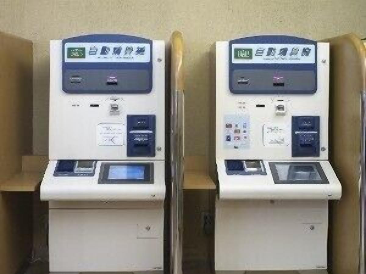Two identical self-service kiosks with digital displays, card slots, and a cash drawer.