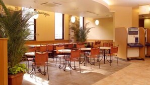Ein Hotelrestaurant mit runden Tischen und orangefarbenen Stühlen, Zimmerpflanzen und einer Selbstbedienungsgetränkeautomaten.