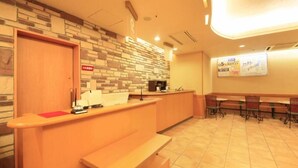Ein Empfangsbereich mit Theke, einer Holzbank, einer Wand mit Mosaikmuster und einem Informationsbrett.